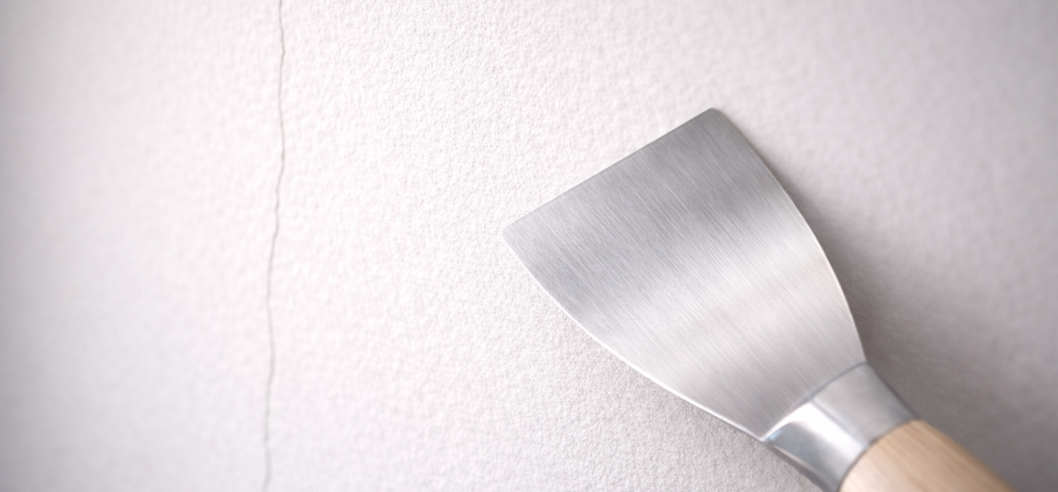 Шпатель у стены с трещиной перед ремонтом поверхности