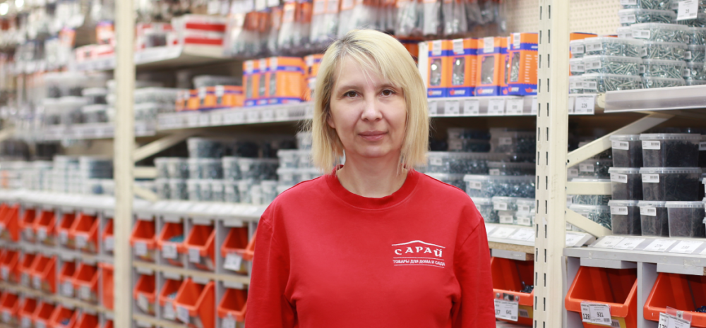 сотрудник магазина сарай в отделе крепежа на фоне стеллажей с метизами