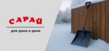 Снеговая лопата с деревянной ручкой и ребрами жёсткости прислонена к деревянному забору на заснеженном дворе частного дома ранним утром